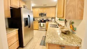A kitchen with wooden cabinets, a stainless steel refrigerator, a microwave, an oven, and granite countertops. - #631 Beautiful poolside Condo perfect for a family getaway (Harrison County)