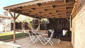 An outdoor patio with a wooden pergola, a hammock, a round table, and a sofa.