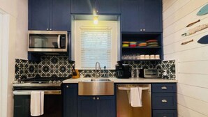 A compact kitchen with dark blue cabinets, a microwave, a stove, a sink, and a dishwasher.