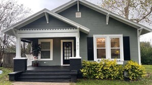 A two-story house with a front porch, a garage, and a small front yard with yellow bushes.