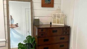 A room with a wooden floor, a large mirror, a wooden dresser, a small plant, and a picture on the wall.