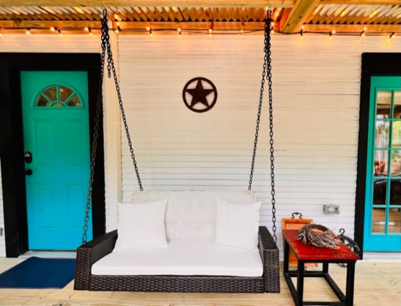 A white sofa swing with a star decoration on the wall, a turquoise door, and a red table with items on it.