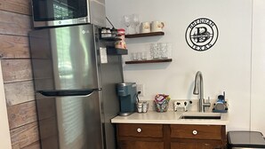 Una cocina compacta con un refrigerador de acero inoxidable, gabinetes de madera, un lavamanos y una cafetera.