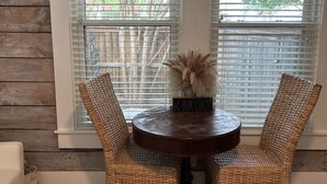 Un comedor con una mesa redonda y dos sillas de mimbre, un jarrón decorativo y un cartel que dice 