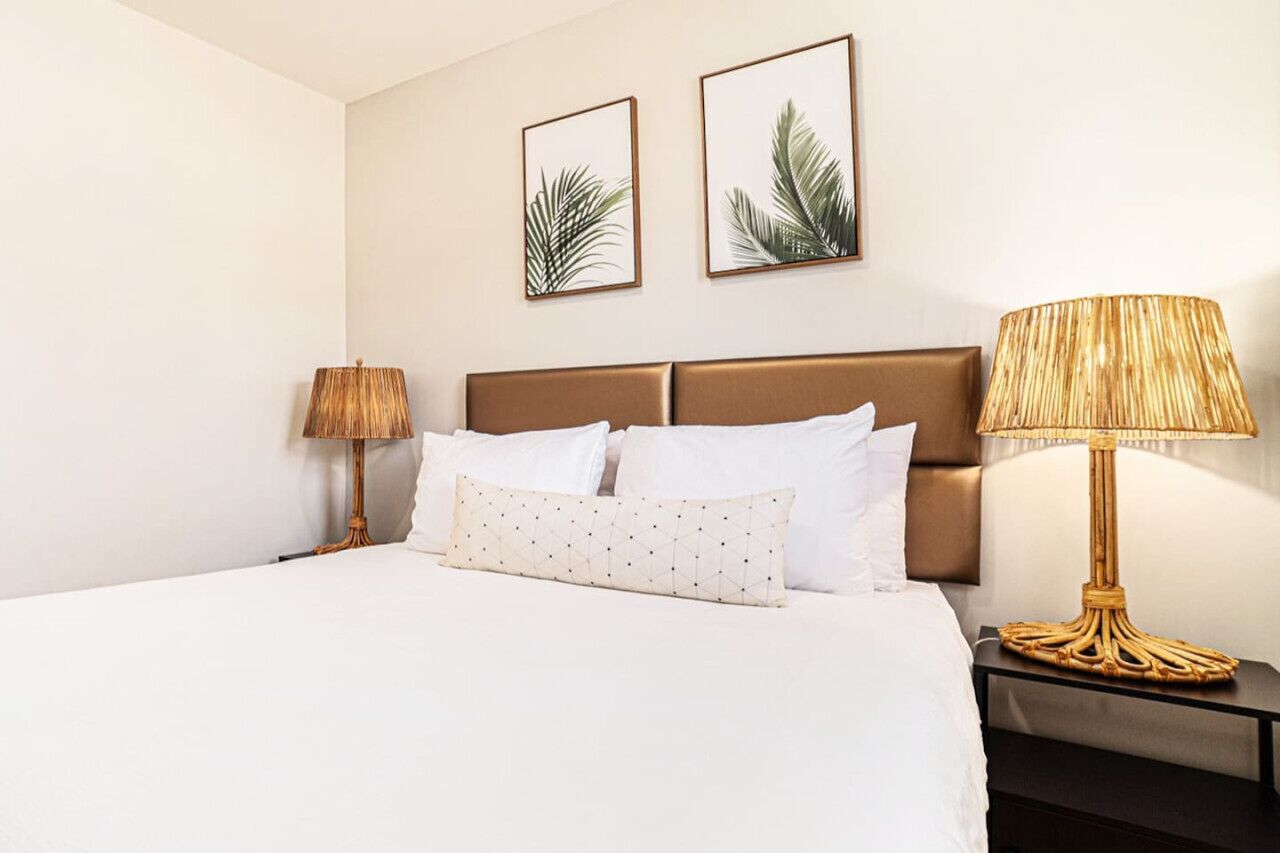 A hotel room with a large bed, two bedside lamps, and two framed leaf artworks on the wall.