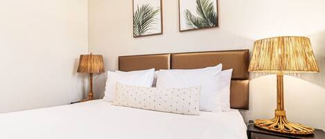 A hotel room with a large bed, two bedside lamps, and two framed leaf artworks on the wall.