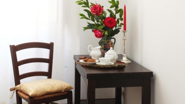 A wooden chair with a cushion, a small table with a vase of red flowers, a candle, and a tray with a teapot, cup, and saucer. - Dimora Pieri - Appartamento Medici, historic building  in the old center with elevator (Firenze)