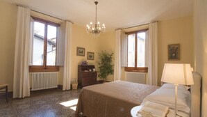 A bedroom with a bed, a nightstand, a lamp, a dresser, a radiator, and two windows with curtains. - Dimora Pieri - Appartamento Medici, historic building  in the old center with elevator (Firenze)