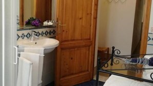 Une salle de bain avec une porte en bois, un lavabo avec un miroir et une étagère en verre où sont posées des serviettes.