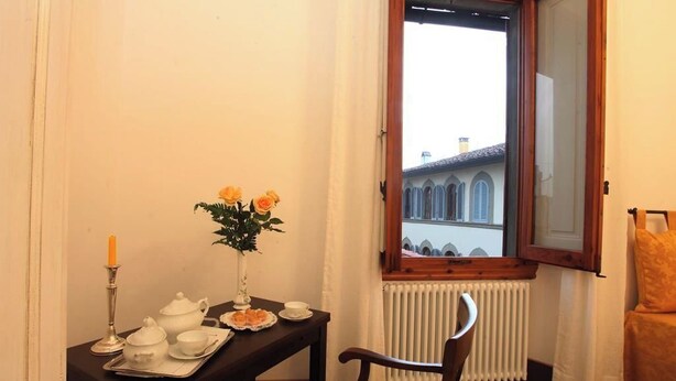 Un coin repas avec une table dressée pour deux personnes, un vase rempli de fleurs et une vue sur un bâtiment par la fenêtre.