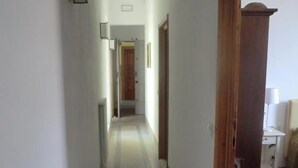 Un couloir étroit avec des carreaux de sol décorés, une chaise en bois et un bureau avec une lampe.