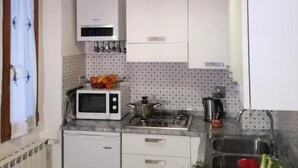 Cocina compacta con armarios blancos, microondas, estufa y pileta.