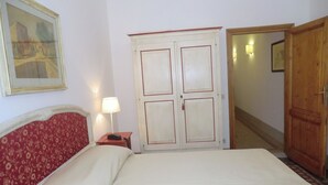 Una habitación de hotel con cama, mesita de noche, lámpara, armario de madera y puerta que da a otra habitación.