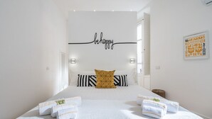 A hotel room with a large bed, a motivational wall art saying "be happy", and a framed picture on the wall.