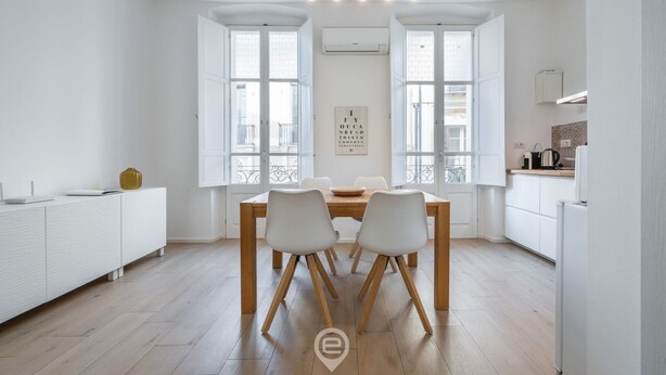 A modern kitchen with white cabinetry, a wooden dining table, and two chairs.