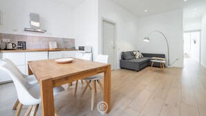 A modern kitchen with white cabinets, a wooden dining table, and a gray sofa in the living area.