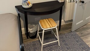 A small room with a black desk, a mirror, a stool, a trash bin, and a patterned rug. - No.4 May Terrace (Inverness)