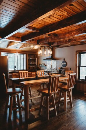 A rustic wooden interior with a large dining table and chairs, a kitchen area with a hanging light fixture, and a 'Kitchen' sign on the wall. - Luxury cabin on private drive. Fall foliage at its finest, waterfront access.  (Remsen)