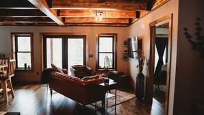 Una sala de estar acogedora con un sofá rojo, piso de madera y ventanas grandes.