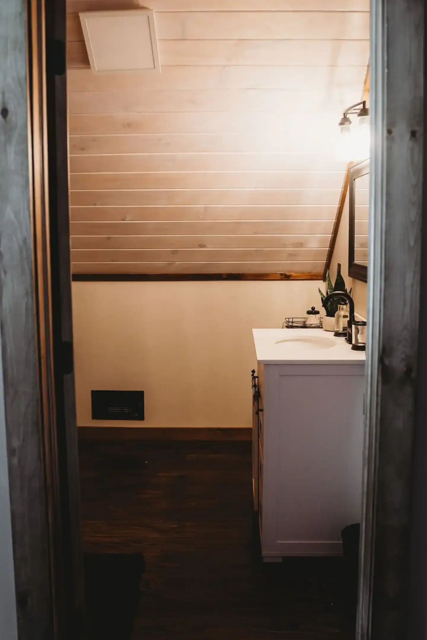 A narrow hallway leading to a bathroom with a white sink, a mirror, and a shower area.