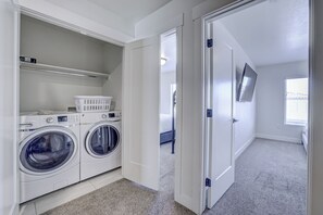 A laundry room with a washing machine and dryer, a shelf with laundry baskets, and a door leading to another room. - Top Tier Townhome in Washington Utah Private Spa, Pool, Firepit. VS507 (Washington)