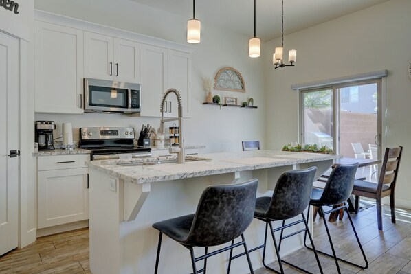 A modern kitchen with white cabinetry, a built-in microwave, a stainless steel range, and a large island with bar stools. - Top Tier Townhome in Washington Utah Private Spa, Pool, Firepit. VS507 (Washington)