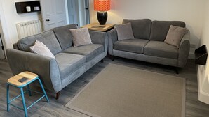 A modern living room with two grey sofas, a small wooden stool, a patterned rug, and a table lamp. - City Apartment - No.1 May Court (Inverness)