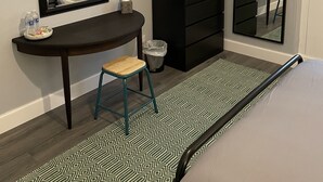 A bedroom with a bed, a vanity with a mirror, a small stool, a black dresser, and a patterned rug. - City Apartment - No.1 May Court (Inverness)