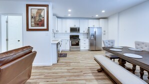A modern kitchen with white cabinets, stainless steel appliances, and a wooden dining table with white plates. - Spacious La Plata Escape (La Plata)