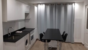 Una cocina moderna con armarios blancos, una encimera negra, un lavamanos y una lavadora, además de una mesa de comedor con sillas.