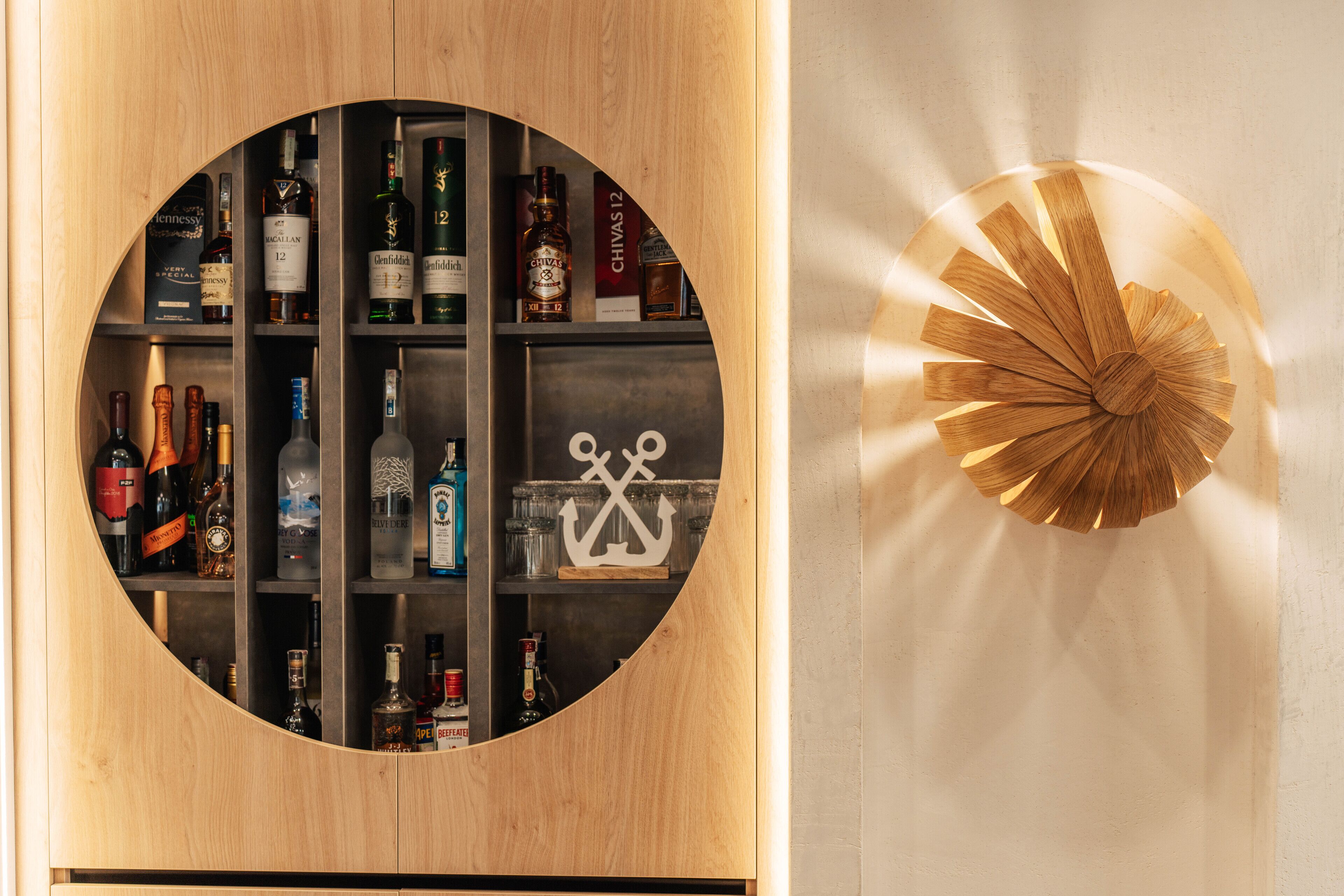 Un estante de madera circular con varias botellas de licor y un adorno con forma de ancla.