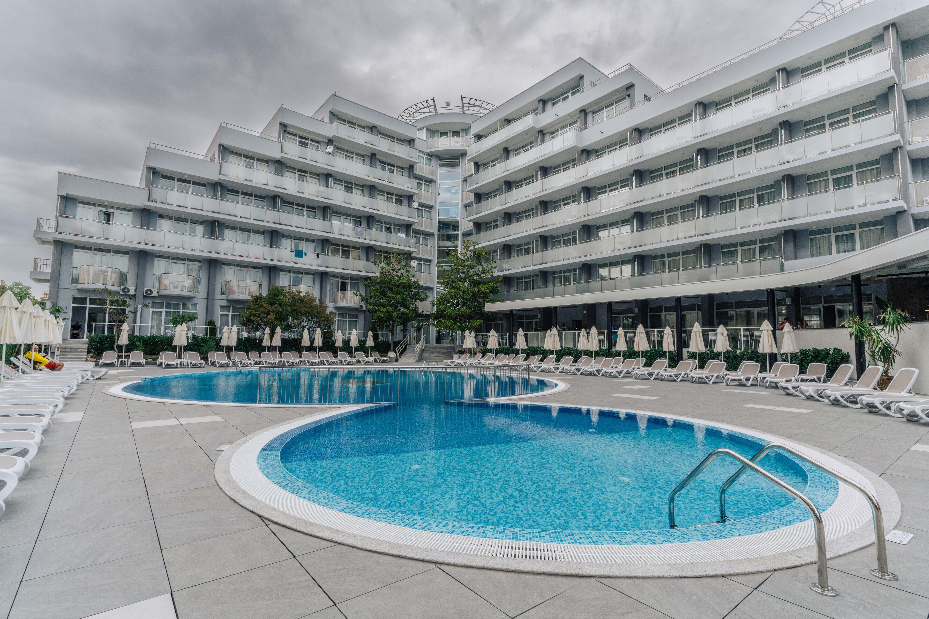 A modern hotel with a central swimming pool, multiple balconies, and sun loungers.