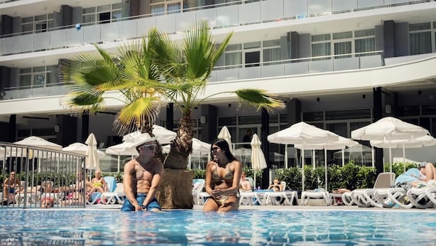A pool area with lounge chairs, umbrellas, and a palm tree. - TUI SUNEO PERLA ADULTS ONLY (Sunny Beach)