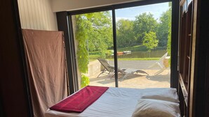 A bedroom with a bed, a view of a garden, and a pool area. - Gîte au Bord de l' eau Proche du Puy du Fou et du Parc Oriental de Maulévrier ! (Maulevrier)