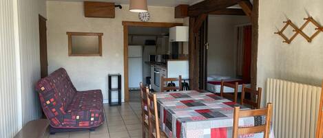 A compact living space with a dining table, a sofa, a kitchen area, and a bed.