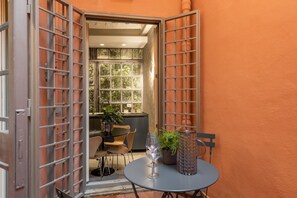 An open door leading to a room with a table, chairs, a potted plant, and a glass of wine. - iFlat | Spanish Steps Delight La Stegiosa (Roma)