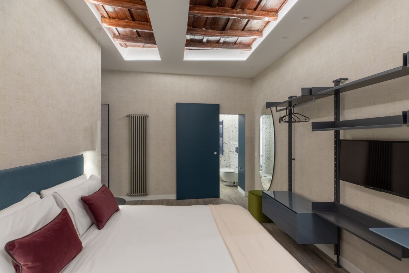 Une chambre d’hôtel moderne avec une lucarne, un lit avec des oreillers, une armoire et une salle de bain visible à travers une porte ouverte.