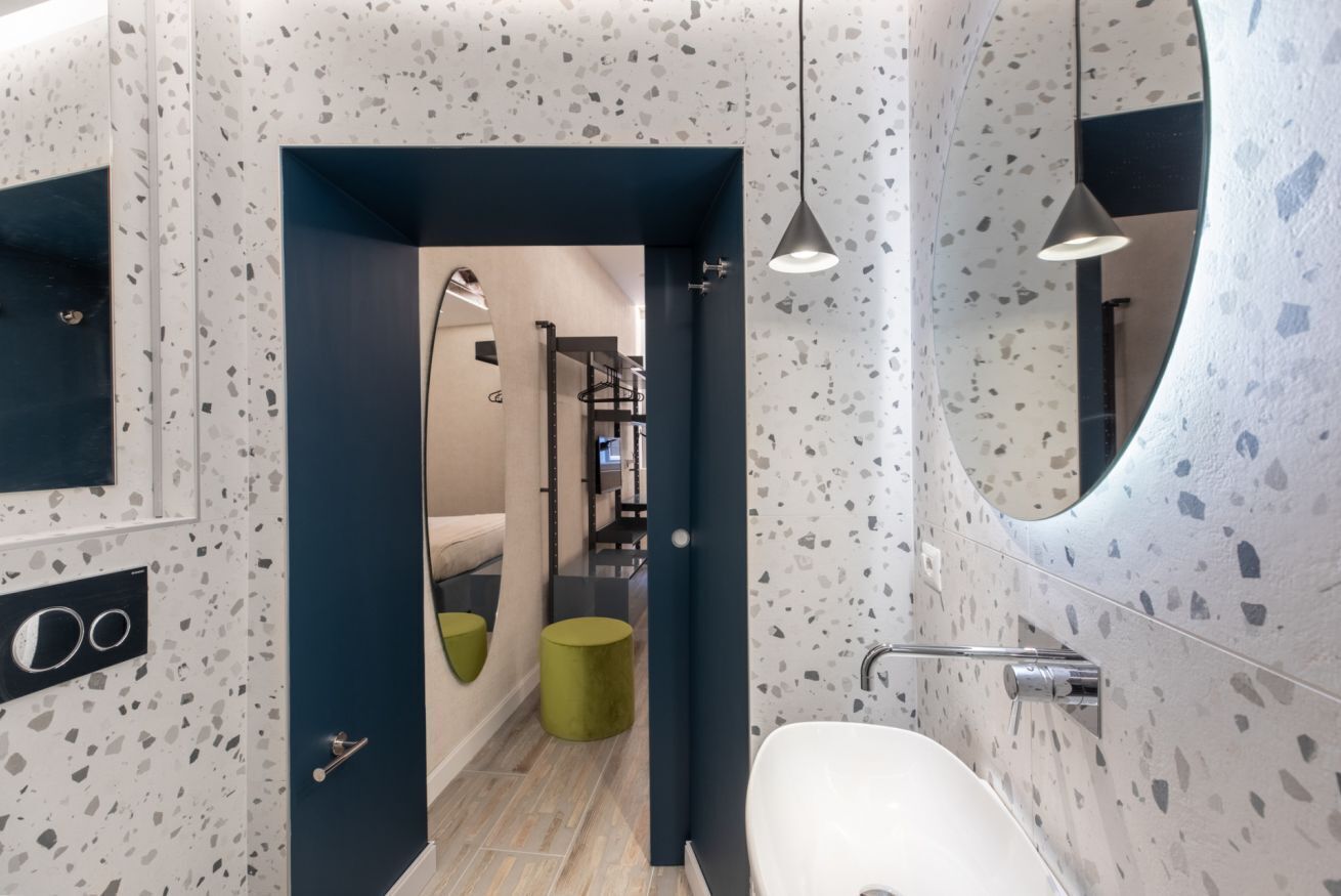 Un baño moderno con lavamanos blanco, un espejo grande y suelo de terrazo.
