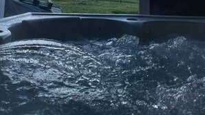 A hot tub with a view of a grassy field and a partly cloudy sky.