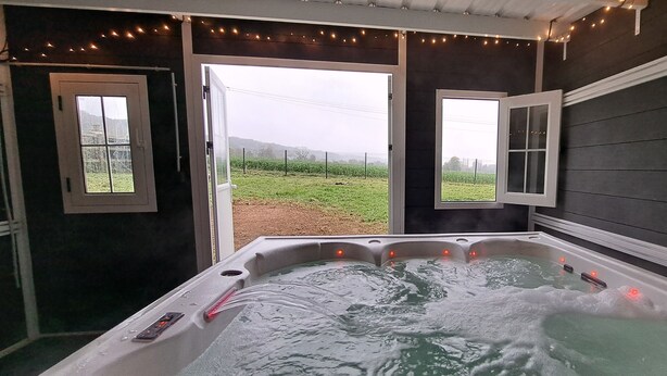 A hot tub with a view of a field through open doors.