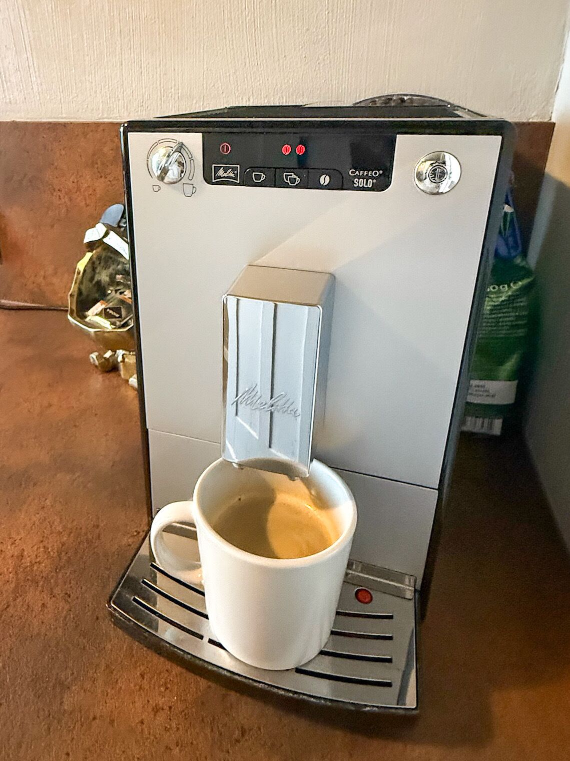 A coffee machine with a cup placed underneath the spout, a control panel with buttons, and a brand name on the machine.