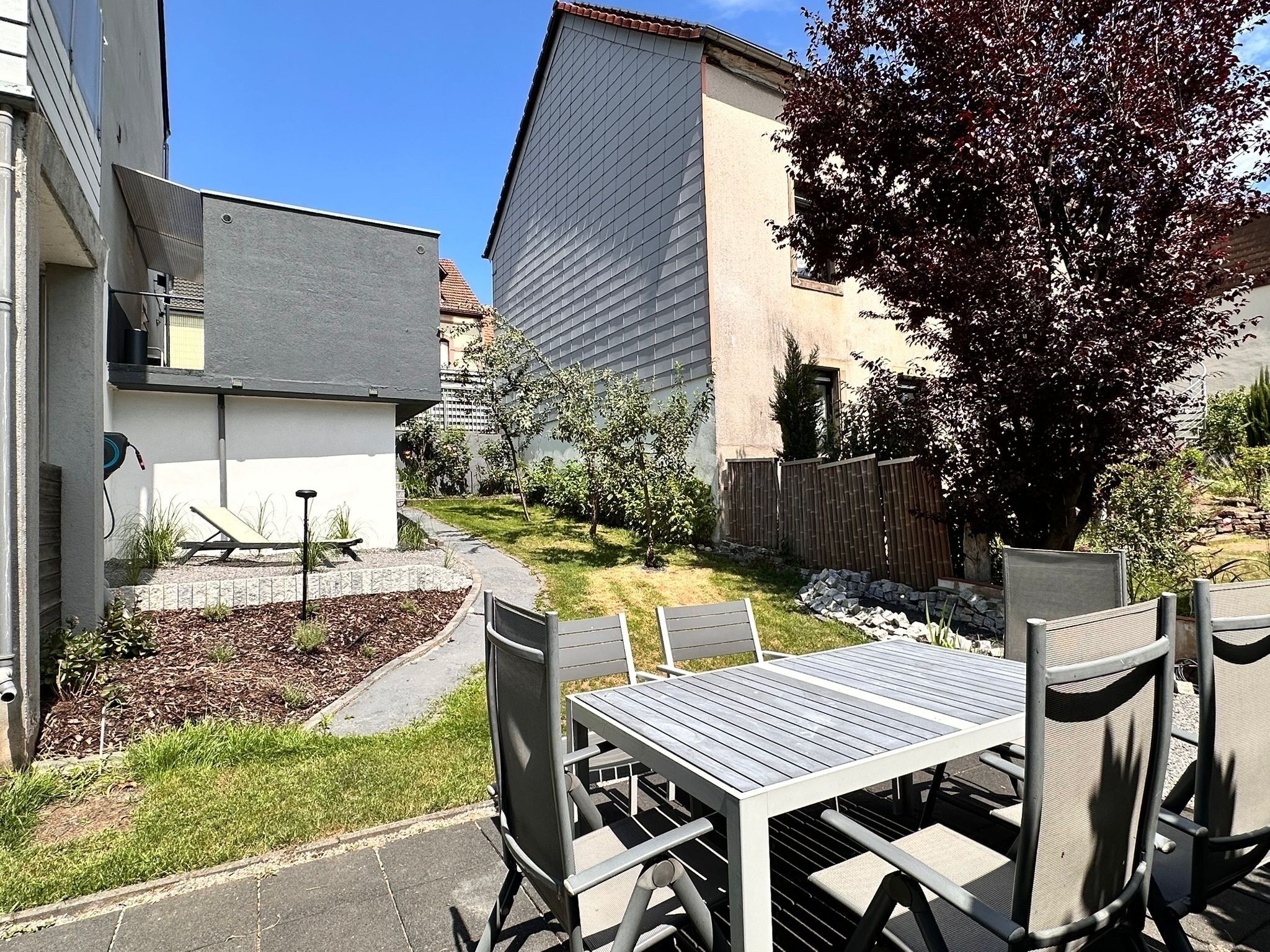 A patio area with a table and chairs, surrounded by a garden and a wooden fence.