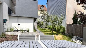 Eine Terrasse mit Holztisch und Stühlen, umgeben von einem Garten und einem Zaun.