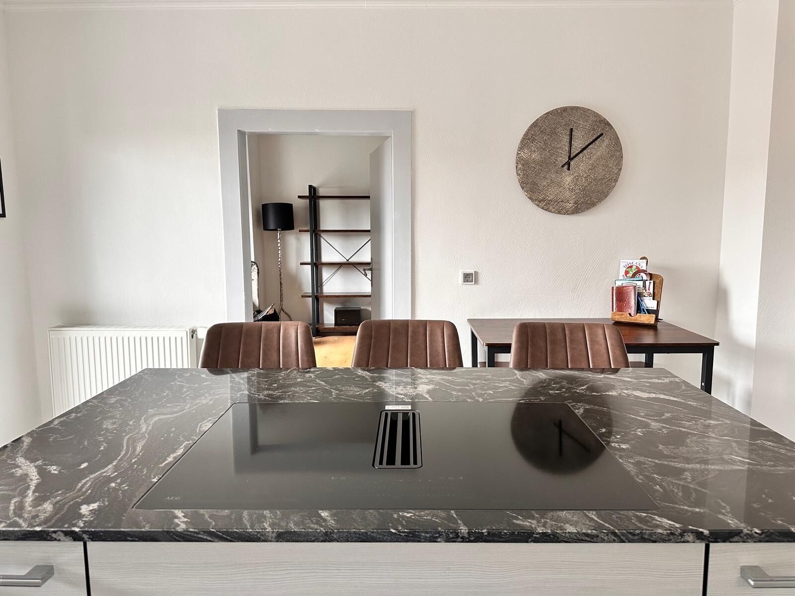 A modern kitchen with a marble countertop, a built-in stove, and a dining area with two chairs and a table.