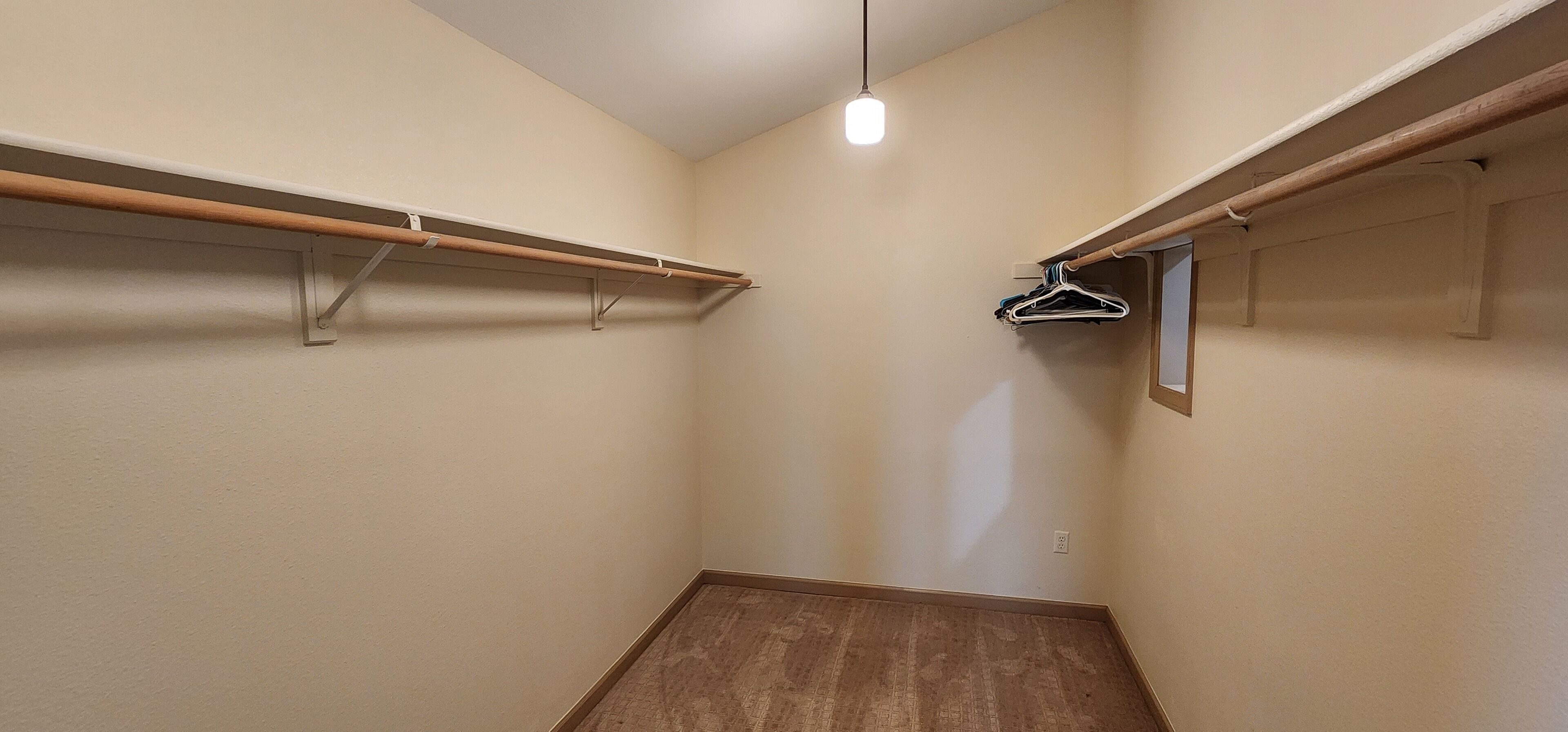 A small, narrow closet with wooden shelves and a hanging rod, featuring a light fixture above.