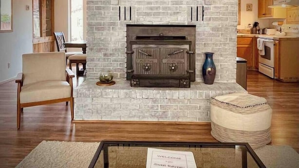 A living room with a brick fireplace, wooden furniture, and a kitchen in the background. - Enjoy a Sweet Retreat in Kanab, Utah. Walking distance to all downtown Kanab has to offer. Close to Zion, Bryce Canyon, and the Grand Canyon! (Kanab)