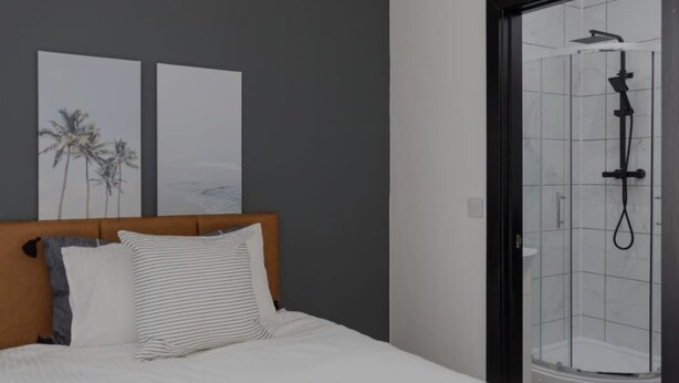 A bedroom with a bed, a headboard, a shower enclosure, and two wall-mounted artworks. - The Residency Rooms Liverpool  (Wallasey)