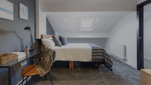 A bedroom with a sloped ceiling, a bed with pillows, a desk with a lamp, and a radiator. - The Residency Rooms Liverpool  (Wallasey)