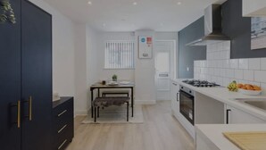 A modern kitchen with a dining area, featuring a dark blue cabinet, a white countertop, and a gas stove. - The Residency Rooms Liverpool  (Wallasey)