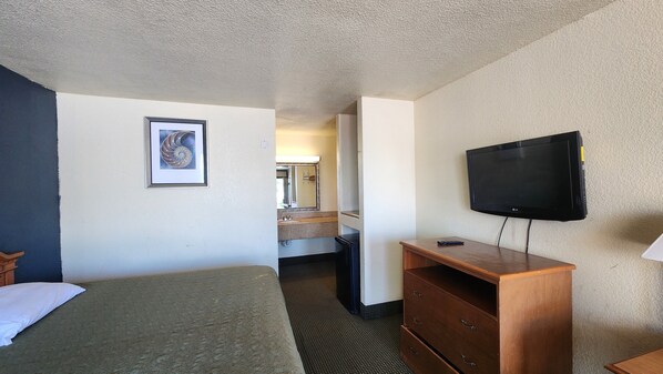 A hotel room with a bed, a dresser, a television, and a bathroom visible through an open door.